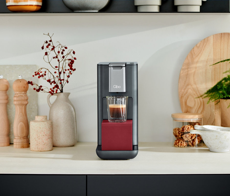 Une machine à café Qbo ESSENTIAL Dark Berry avec une tasse de café sur un comptoir de cuisine.