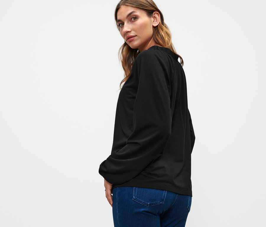 Femme regardant par-dessus son épaule portant une blouse noire avec fronces et un jean.