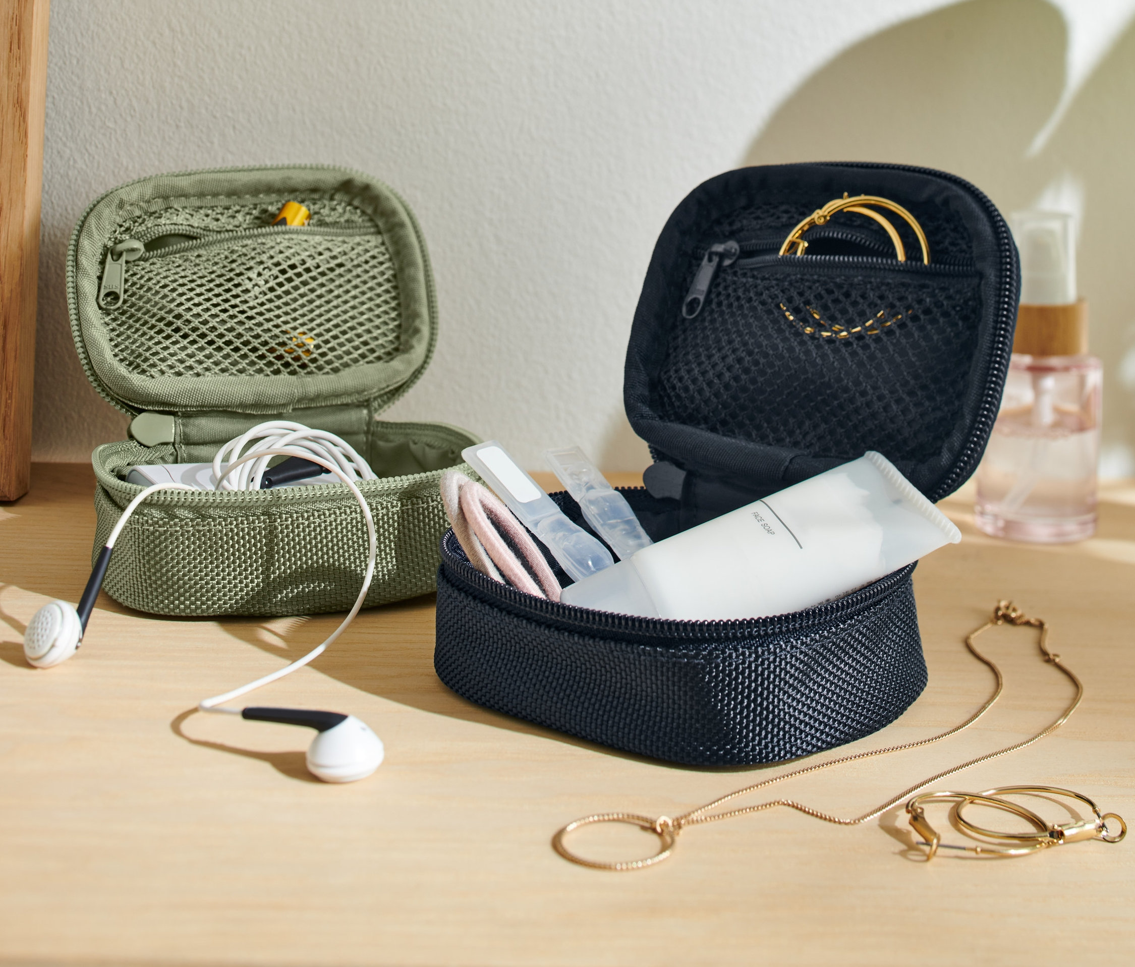 Deux mini-trousses de voyage, une vert olive avec des écouteurs et une bleu marine avec des cosmétiques et des bijoux.