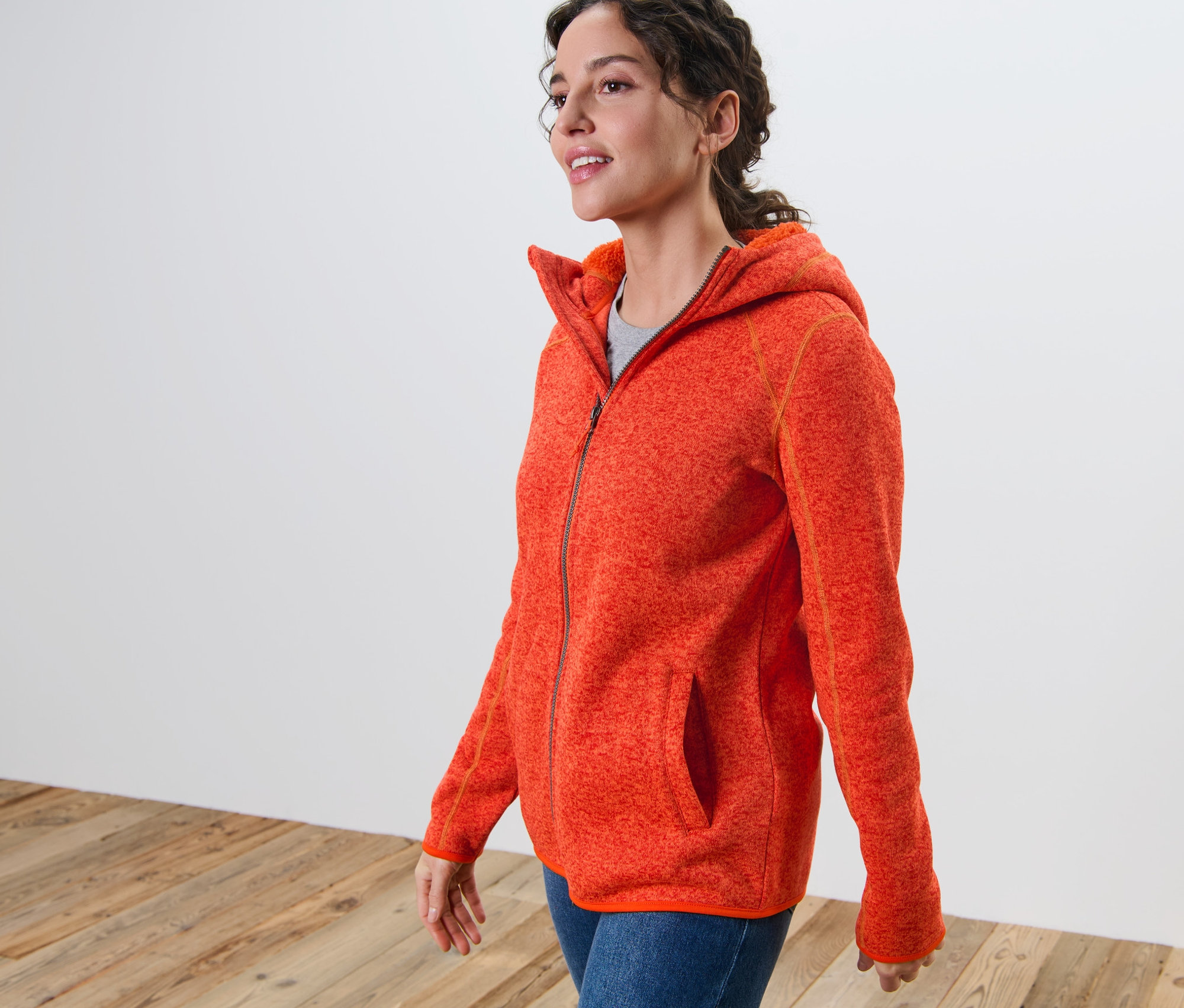 Femme portant une jaquette en maille polaire à capuche orange chiné.