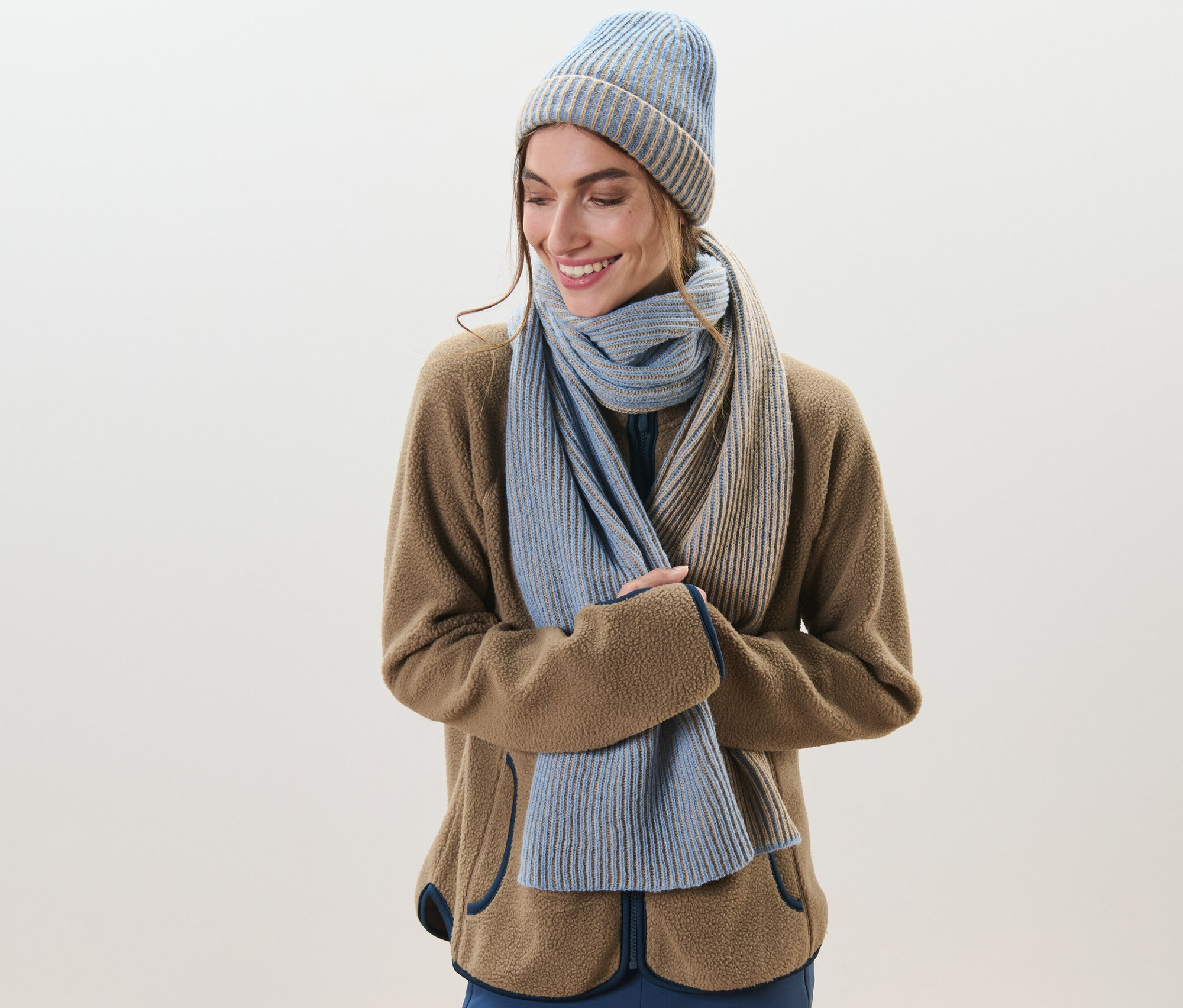 Femme souriant et portant une écharpe en maille et un bonnet.
