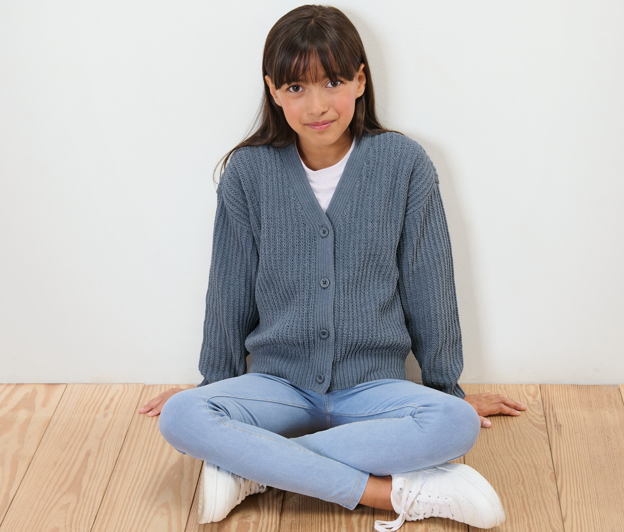 Fille assise par terre portant une veste en tricot chenille bleue pour enfant.