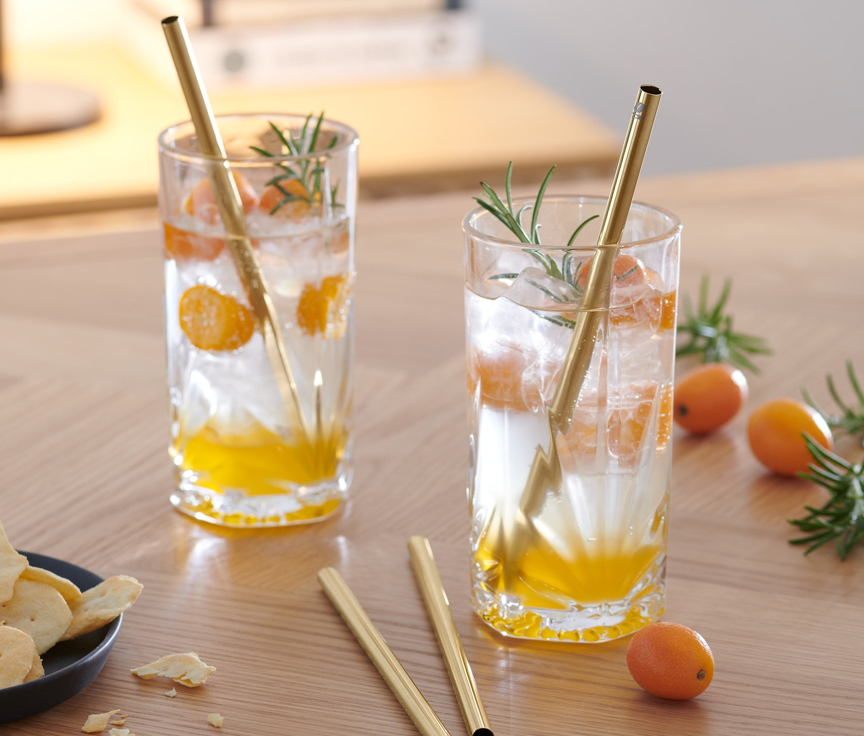 Deux boissons avec des morceaux de fruits et 4 pailles en métal sur une table en bois.