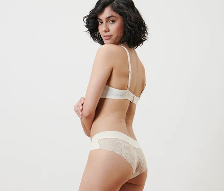 Une femme regardant par-dessus son épaule porte un soutien-gorge couleur crème et 2 slips brésiliens Magic Cut, crème.