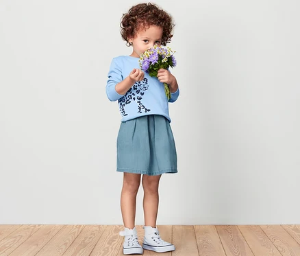 Une fille tient un bouquet de fleurs et porte une jupe en denim pour enfant.