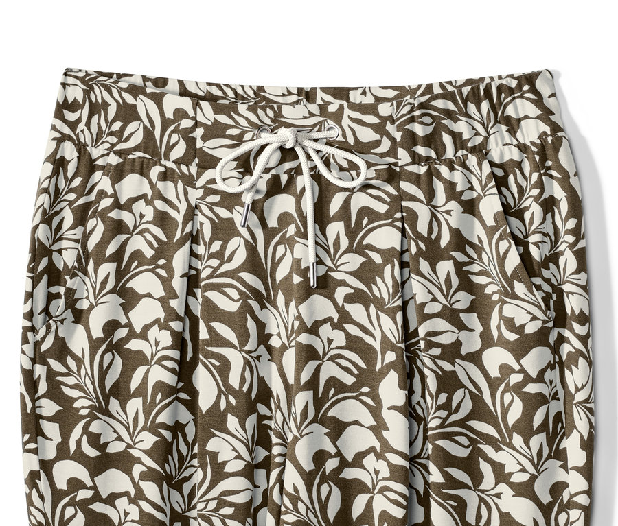 Gros plan d'un pantalon en jersey imprimé avec un motif de feuilles et un cordon de serrage à la taille.
