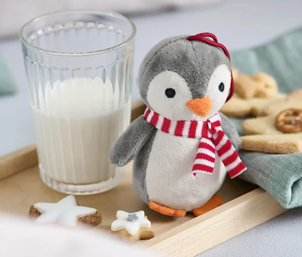 Un pingouin en peluche avec une écharpe se tient à côté d'un verre de lait et de biscuits sur un plateau en bois.