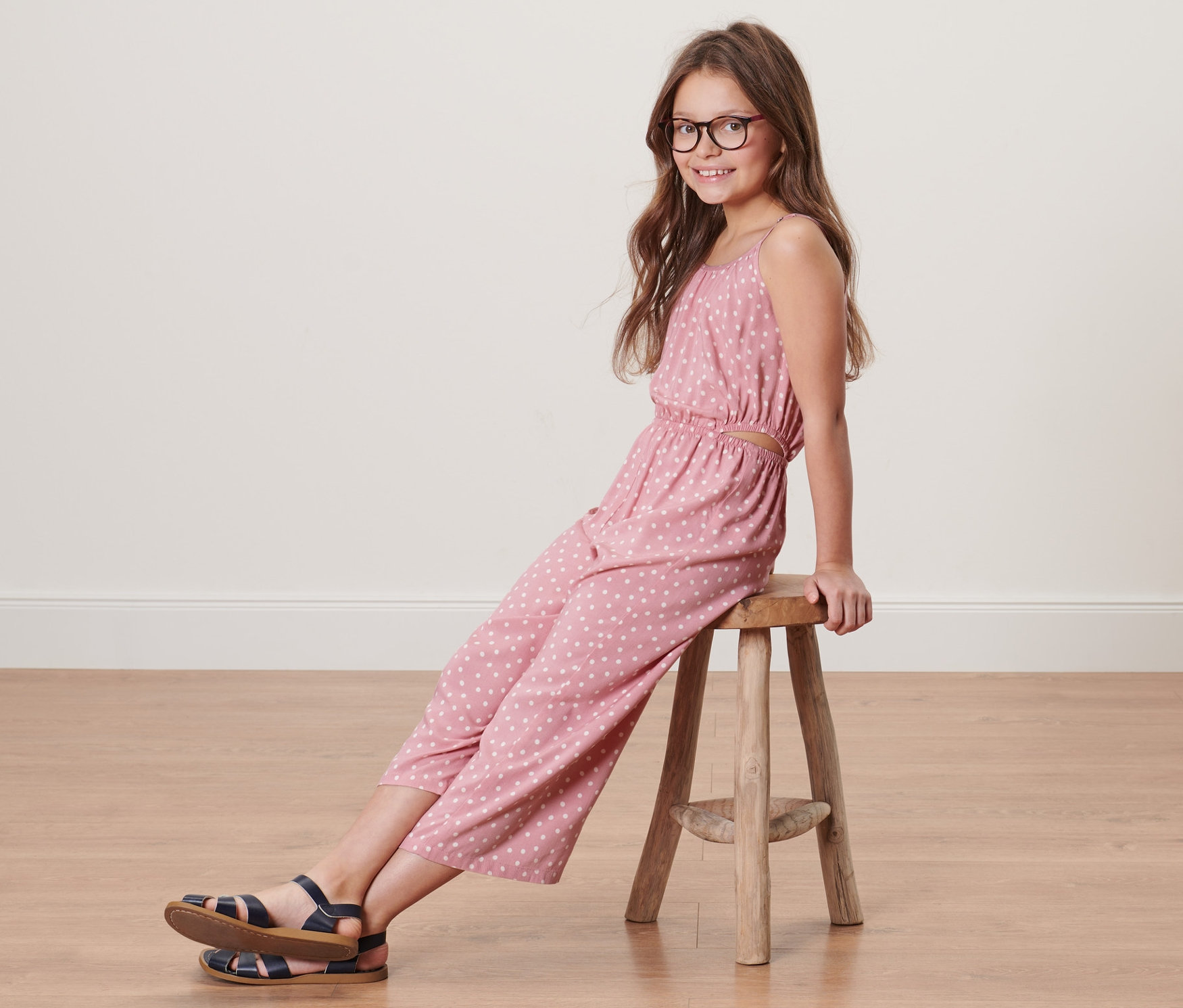 Une fille est assise sur un tabouret et porte une combinaison tissée pour enfants, longueur 7/8.