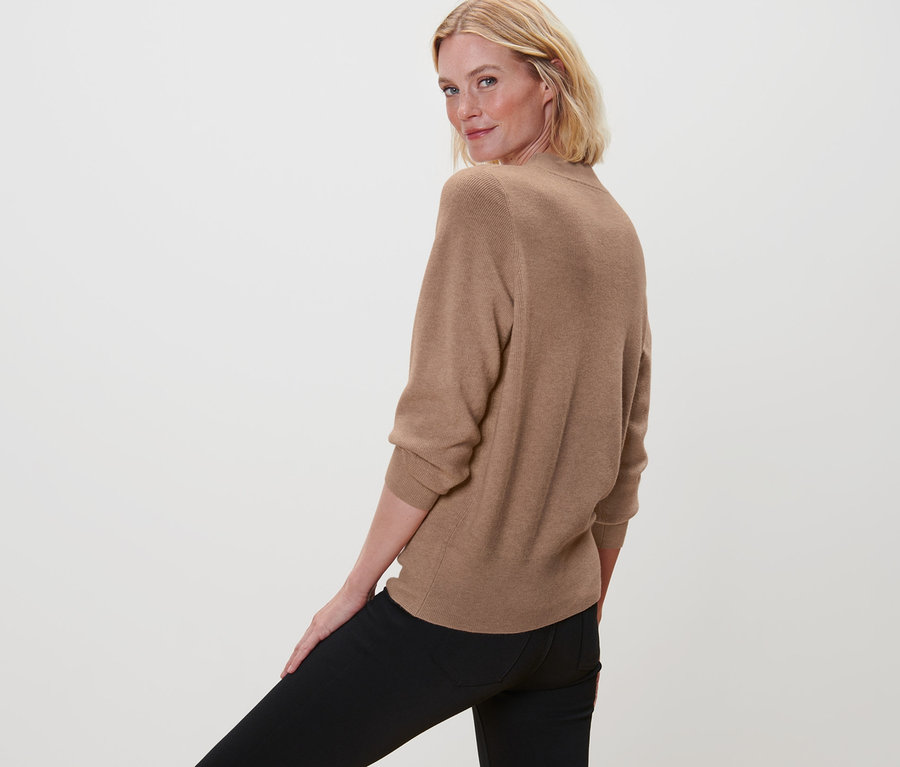 Une femme regarde par-dessus son épaule et porte un pull en maille et un pantalon noir.
