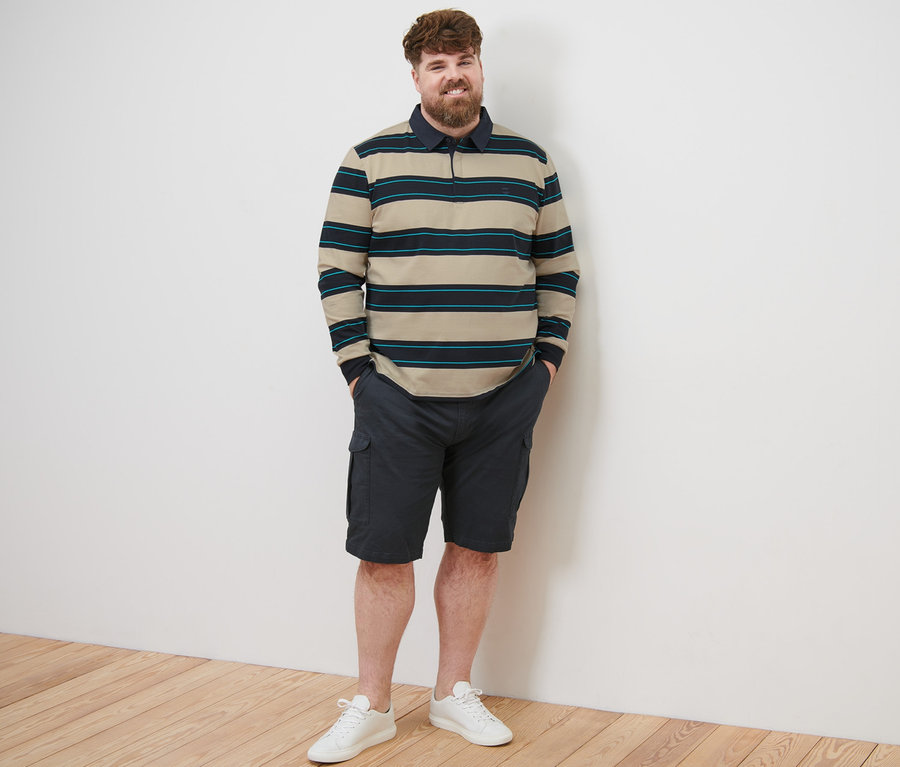 Un homme debout portant un polo à manches longues, un short et des baskets.