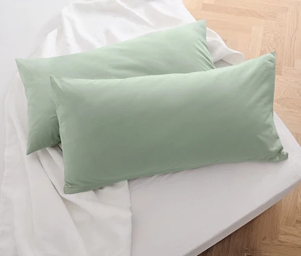 Deux taies d’oreiller en jersey vert sauge sont posées sur un drap blanc.