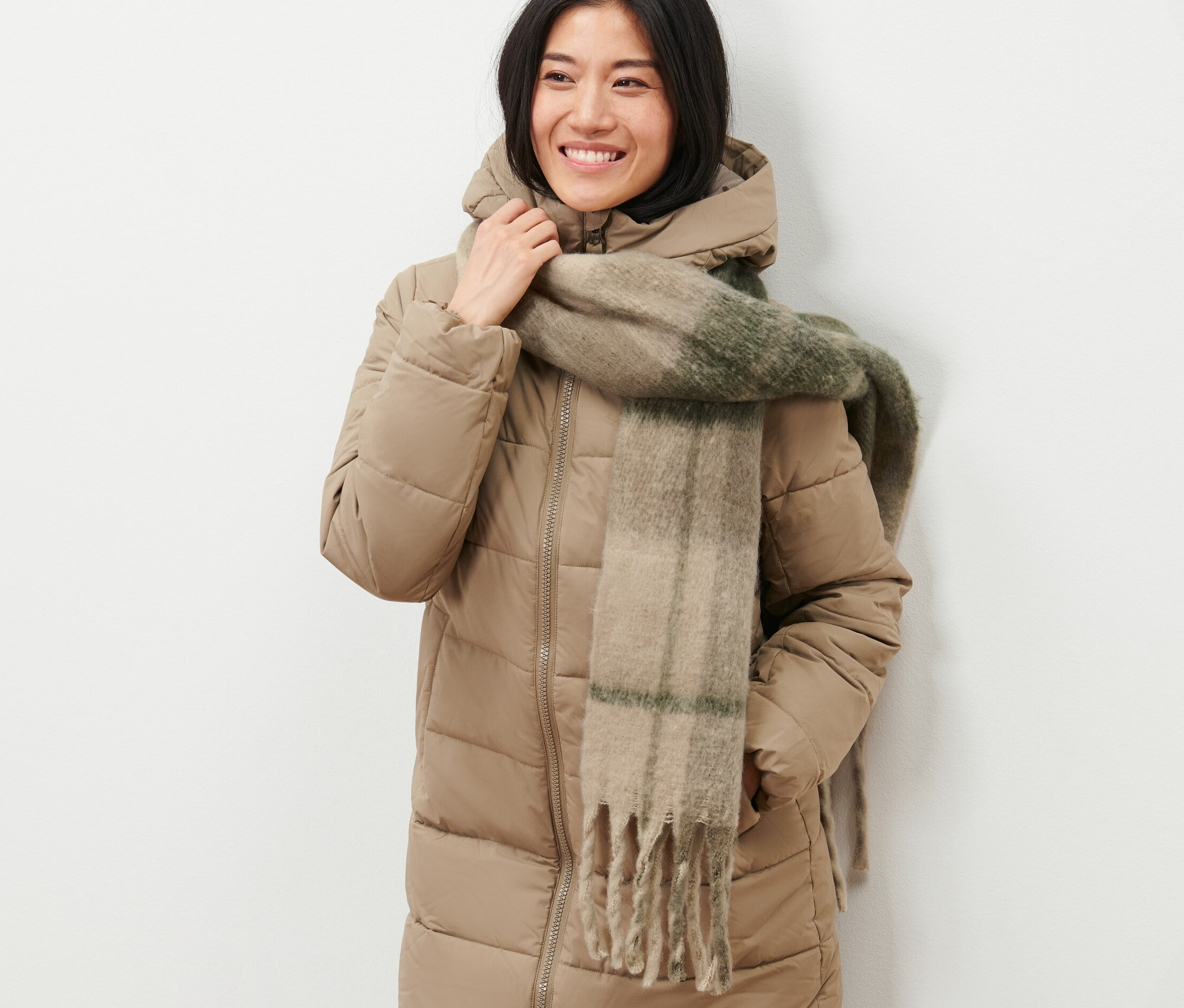 Une femme souriante pose dans une veste beige avec une écharpe en maille.