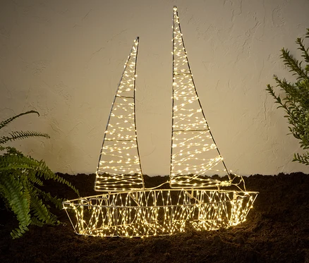 Un bateau d'extérieur 3D à LED illuminé se dresse sur le sol à côté de plantes.