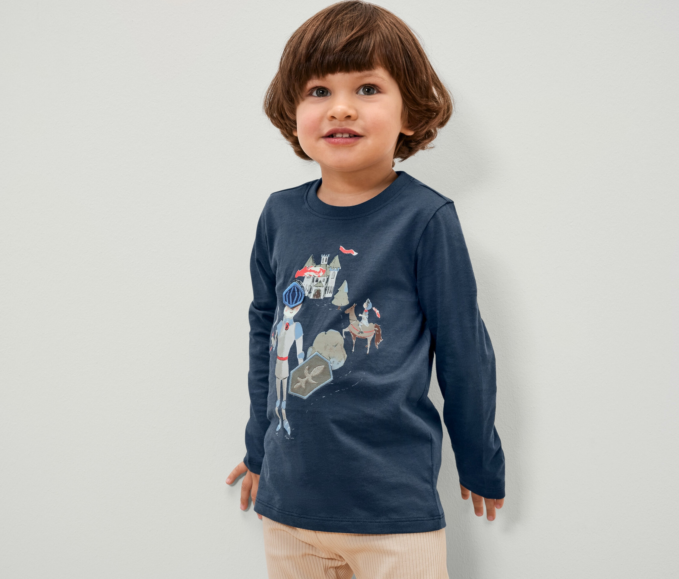 Un garçon porte un t-shirt bleu à manches longues avec un motif de chevalier.