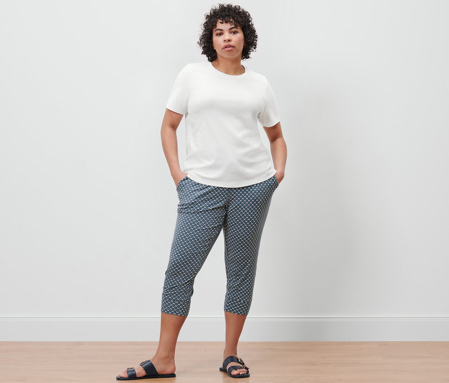 Une femme pose, portant un t-shirt basique crème et un pantalon 3/4 en jersey imprimé.
