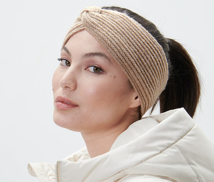 Femme portant un bandeau en maille couleur sable et une veste blanche regardant par-dessus son épaule.