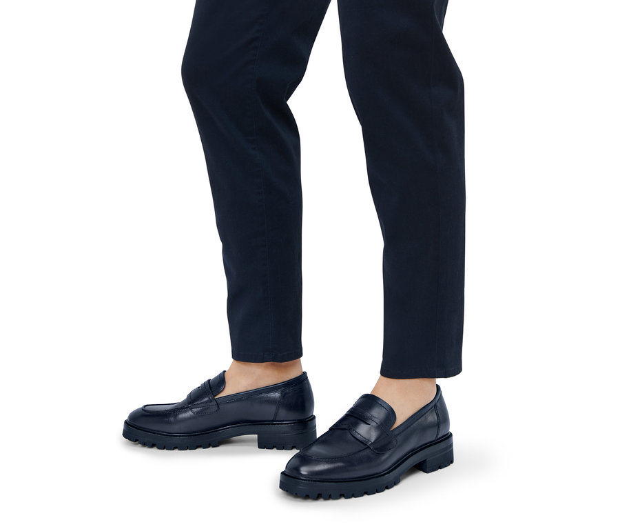 Jambes d'une personne portant un pantalon bleu marine et des mocassins en cuir.