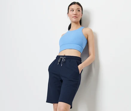 Une femme appuyée contre un mur porte un haut de sport bleu et un short de sport.