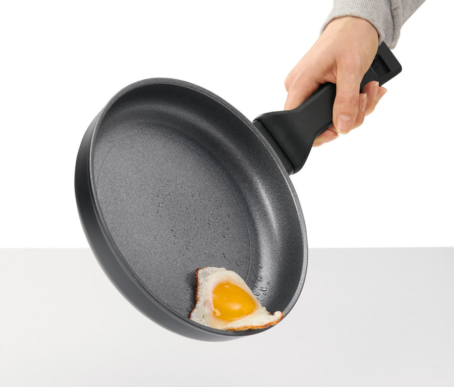 Une main tient une poêle en aluminium avec un œuf au plat.