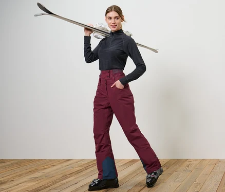 Femme posant en chaussures de ski et pantalon de ski et de snowboard bordeaux.