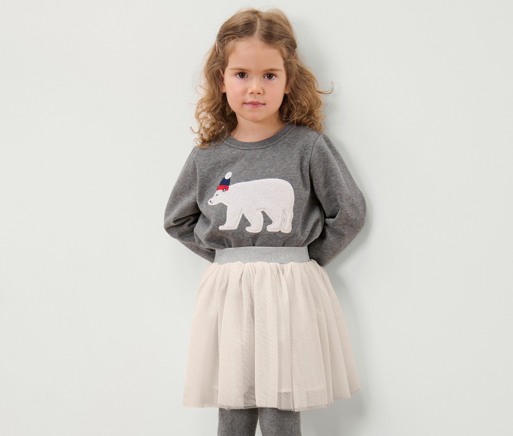 Fillette posant en sweat-shirt gris avec un motif d'ours polaire et jupe en tulle enfant.