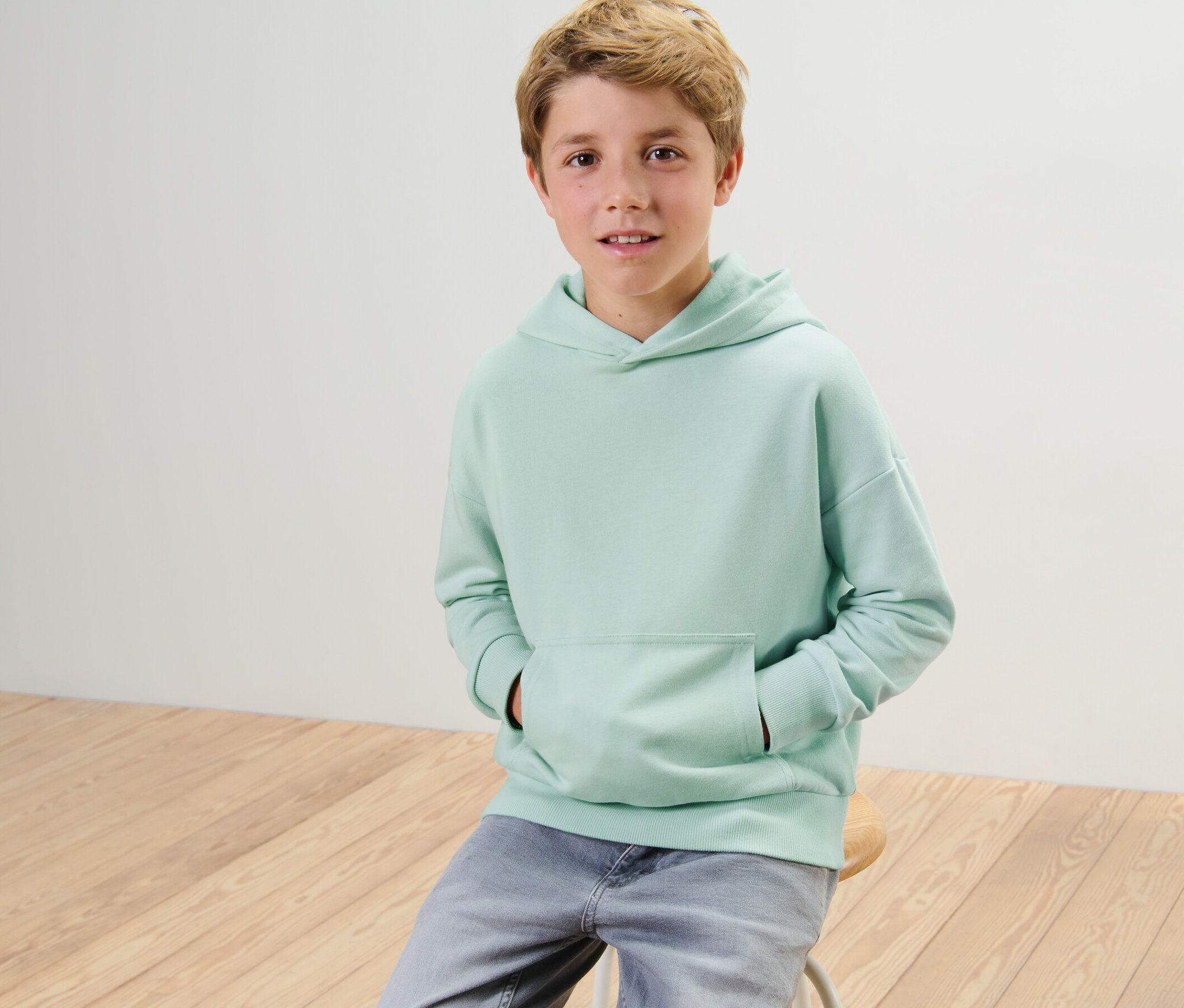 Un garçon est assis sur un tabouret et porte un sweat-shirt à capuche pour enfant.