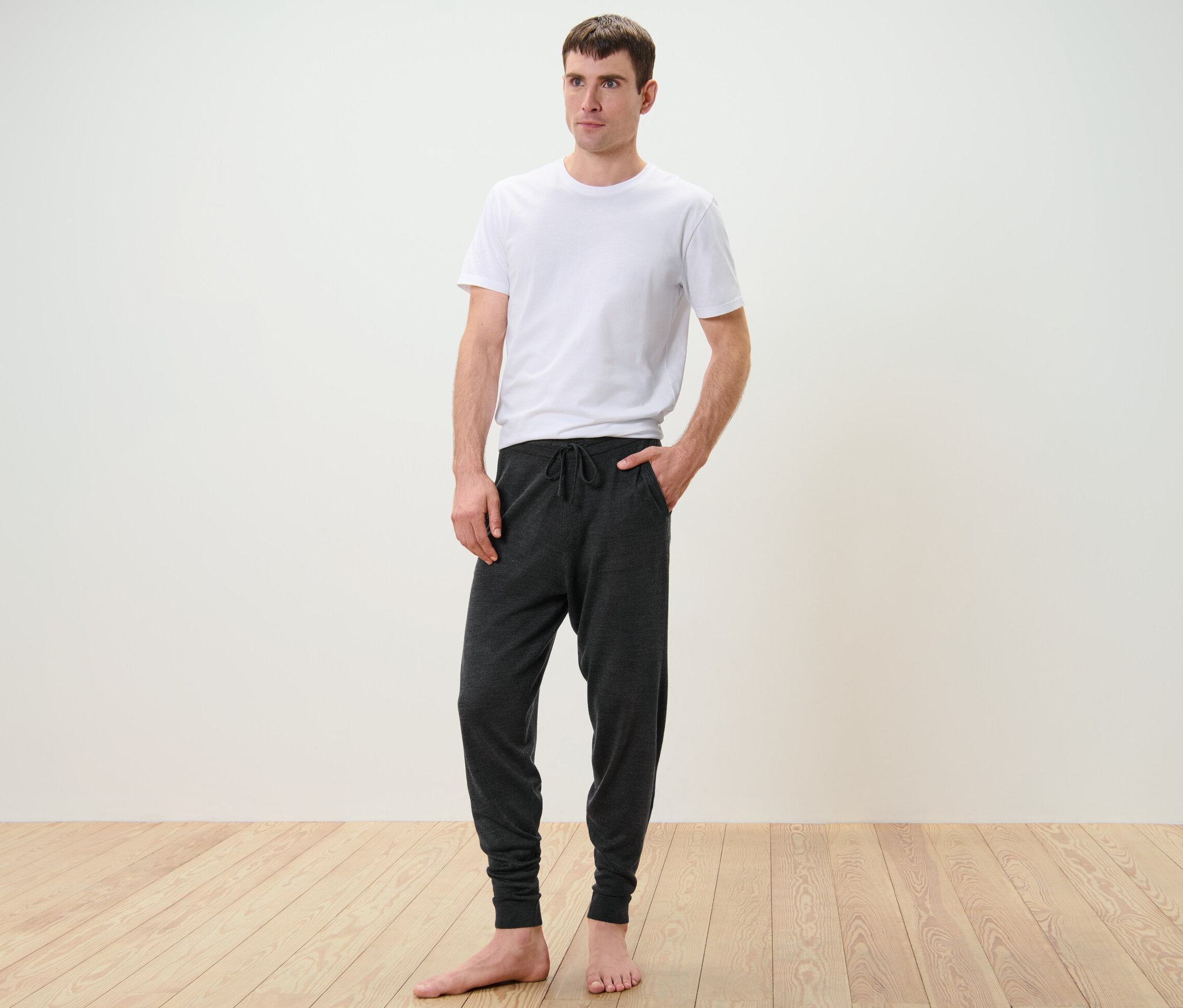 Un homme debout porte un t-shirt blanc et un pantalon home wear à maille fine.