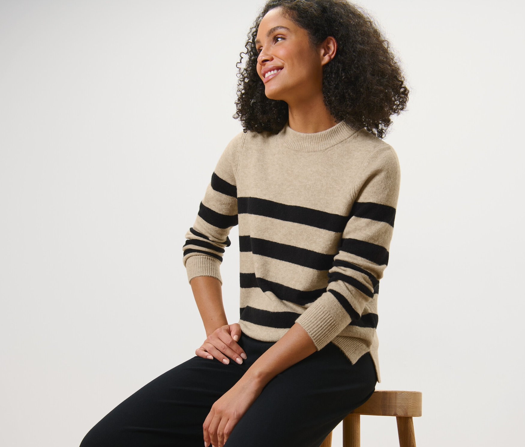 Femme assise sur un tabouret portant un pull en maille à rayures.