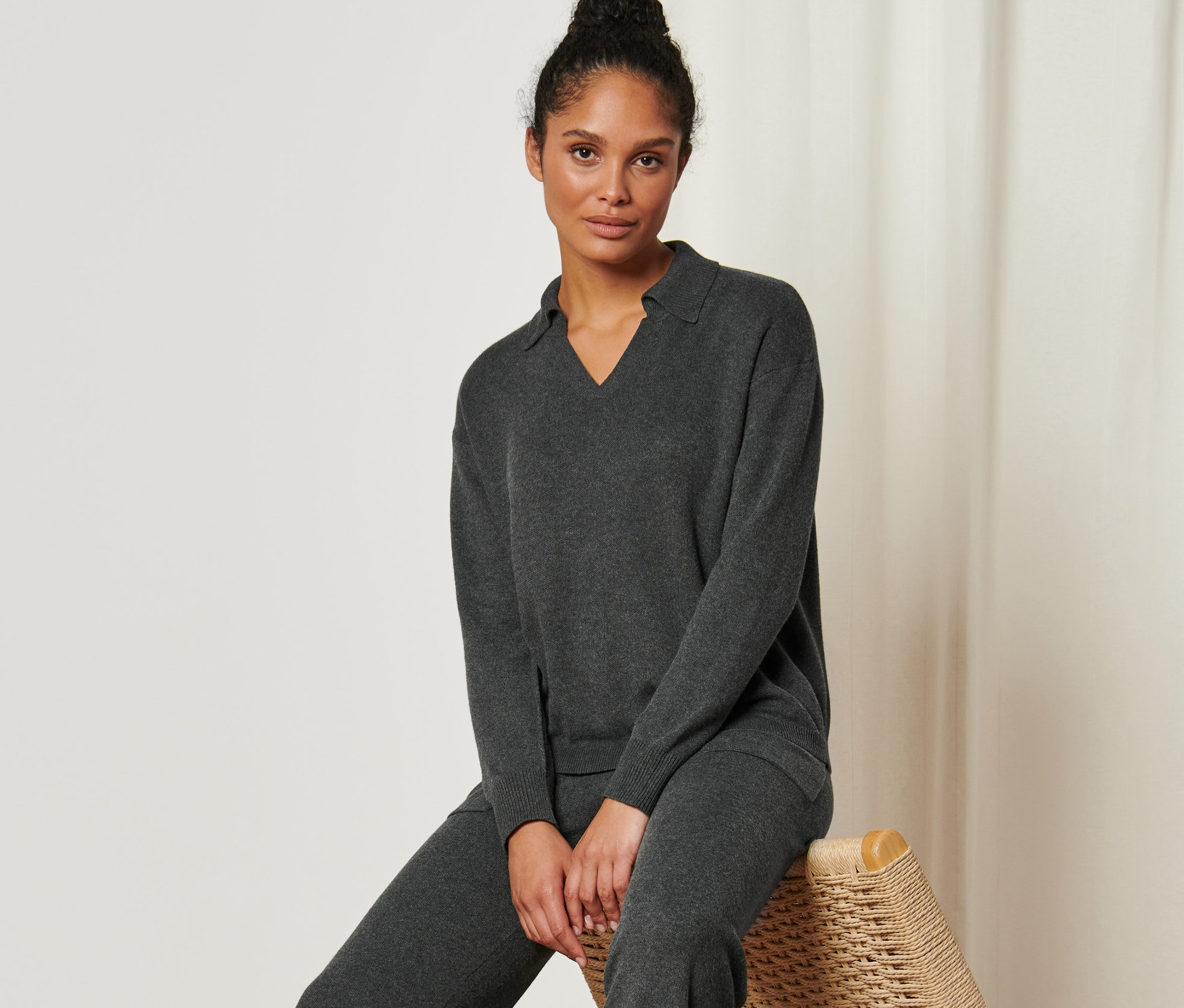 Une femme assise sur une chaise en rotin porte un pull en maille à col polo.