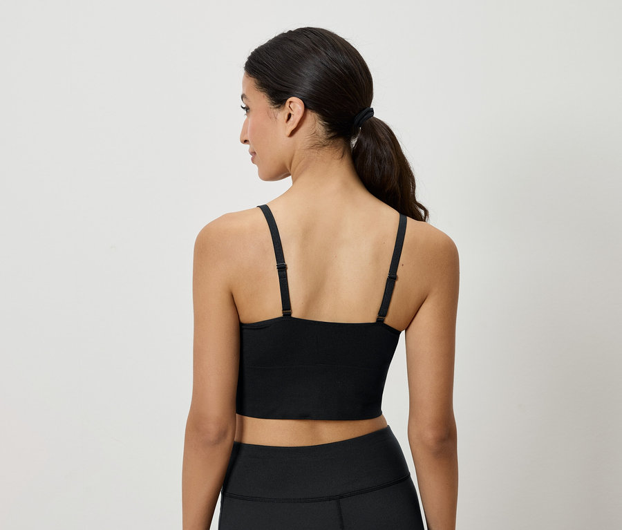 Vue arrière d'une femme aux cheveux bruns attachés en queue de cheval, portant un haut de sport noir et un legging.