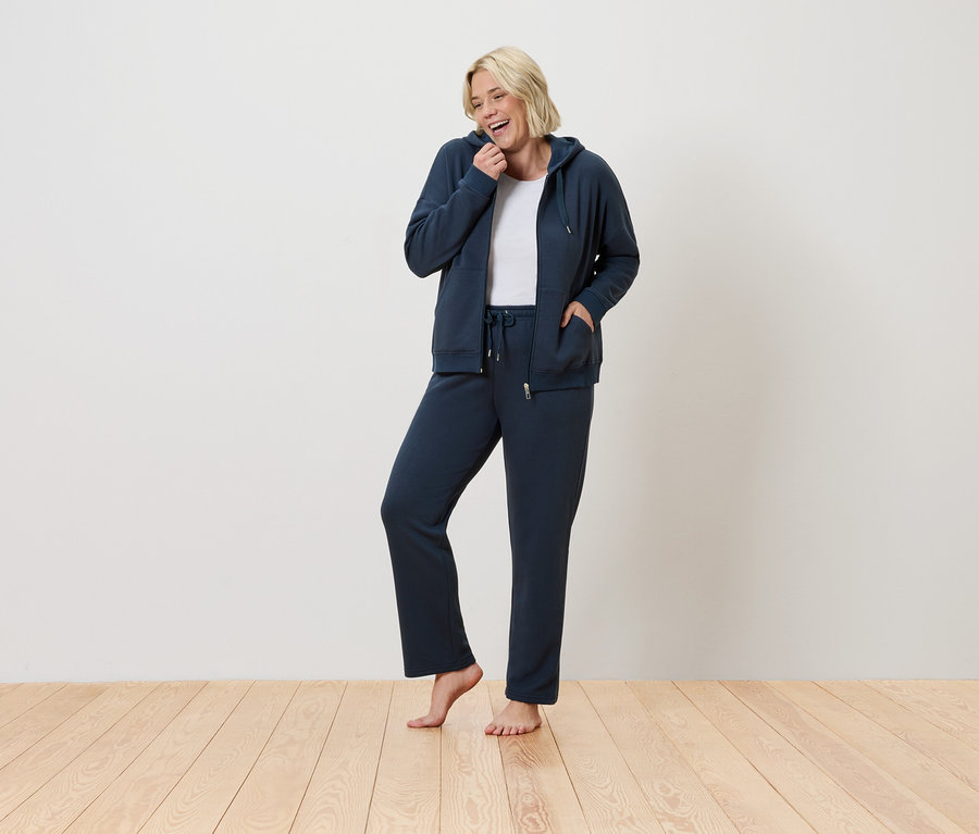 Une femme debout souriant, elle porte un survêtement bleu.