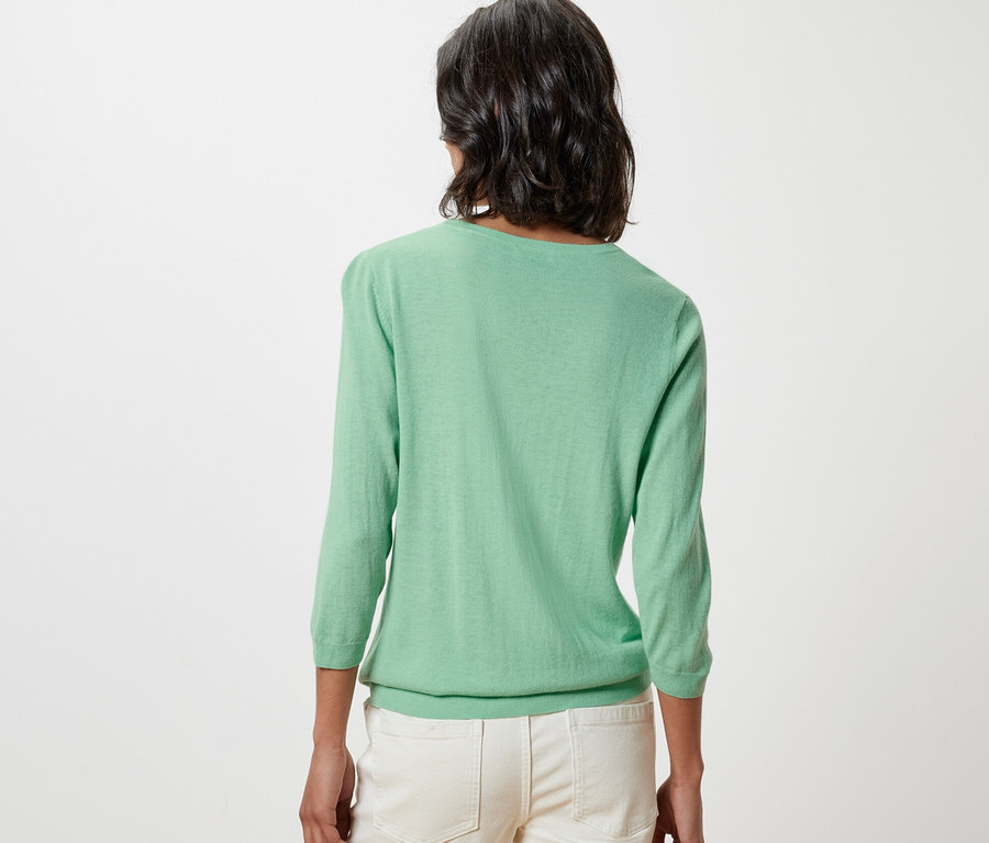 Vue arrière d'une femme portant un pull-over en maille fine vert clair avec de la soie et un pantalon crème.