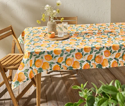 Table avec une nappe lavable à motif d'agrumes, avec un vase de fleurs et des verres d'eau dessus.