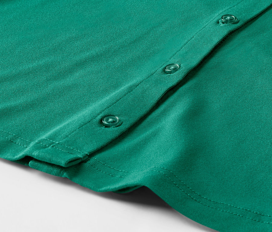 Gros plan sur une blouse émeraude avec patte de boutonnage.