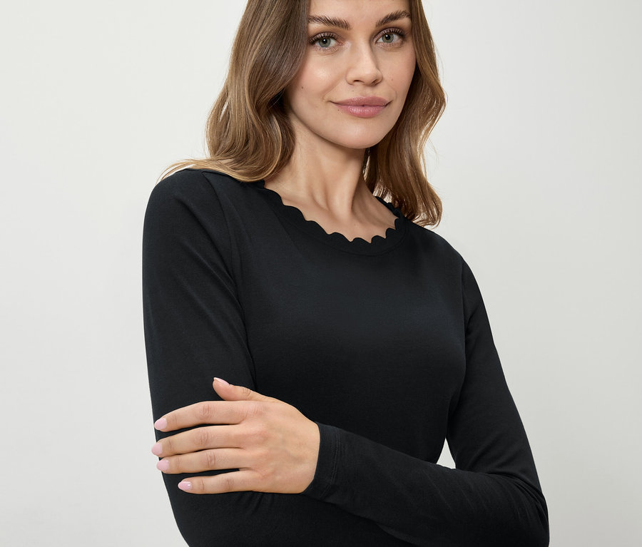 Une femme porte un t-shirt noir à manches longues avec un ourlet décoratif.