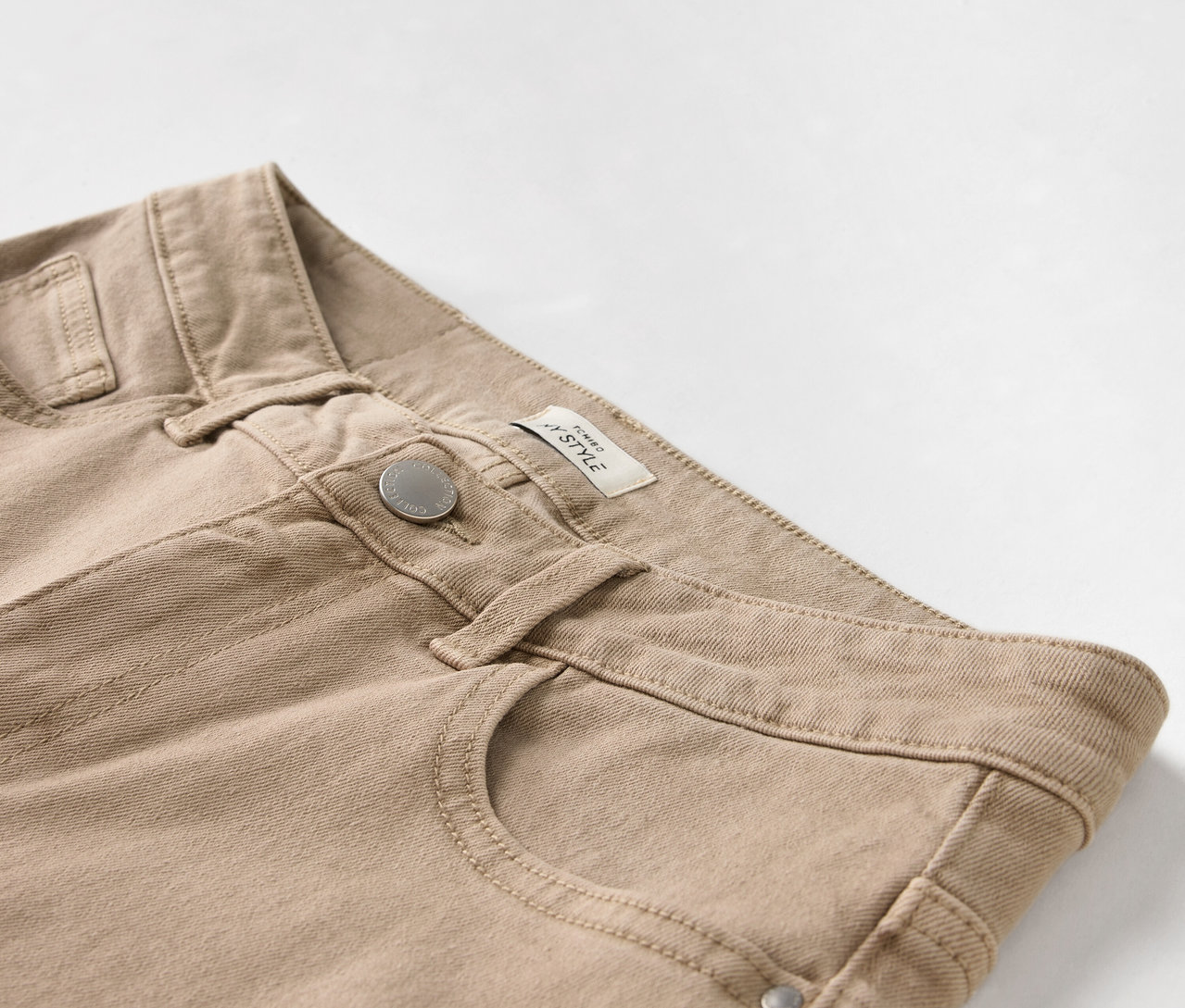 Gros plan d'un pantalon beige avec bouton et poche.