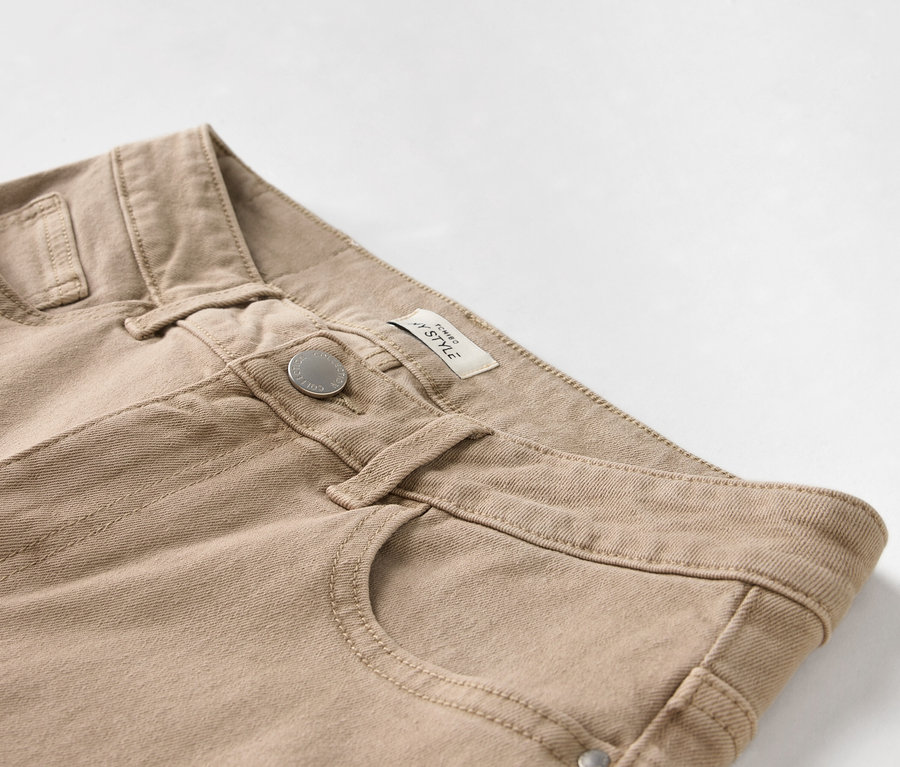 Gros plan d'un pantalon beige avec bouton et poche.