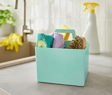 Une boîte turquoise contenant des produits de nettoyage est posée sur un comptoir gris près d'un évier.