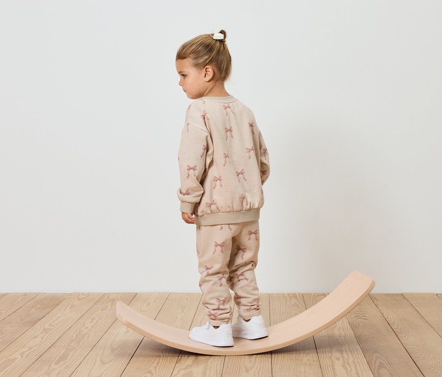 Une fille en survêtement beige se tient sur une planche d'équilibre en bois.
