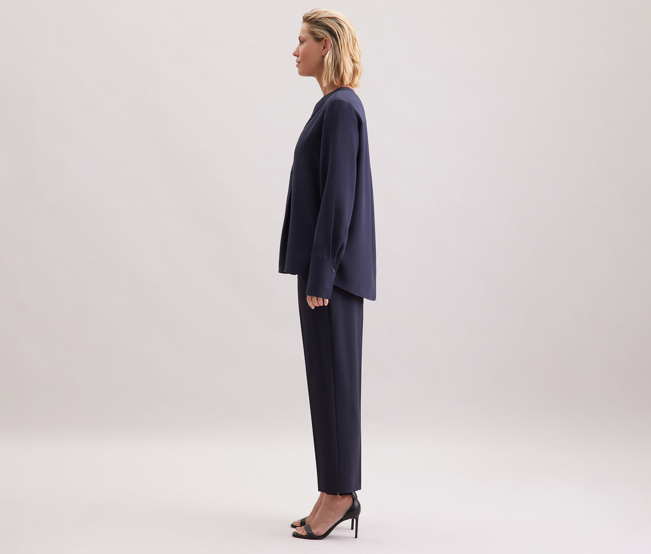 Femme debout de profil portant une tunique en viscose Seidensticker bleu marine, un pantalon et des sandales noires.