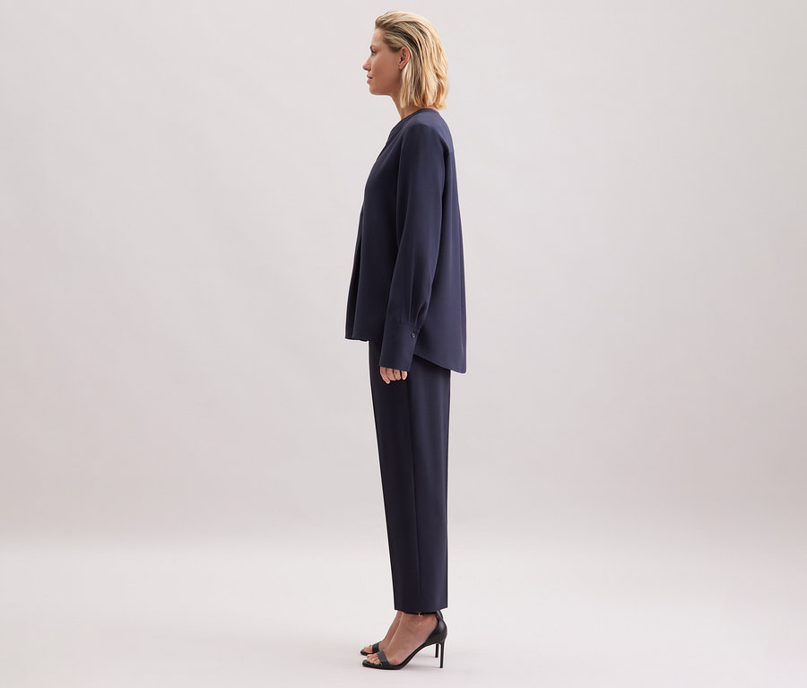 Femme debout de profil portant une tunique en viscose Seidensticker bleu marine, un pantalon et des sandales noires.