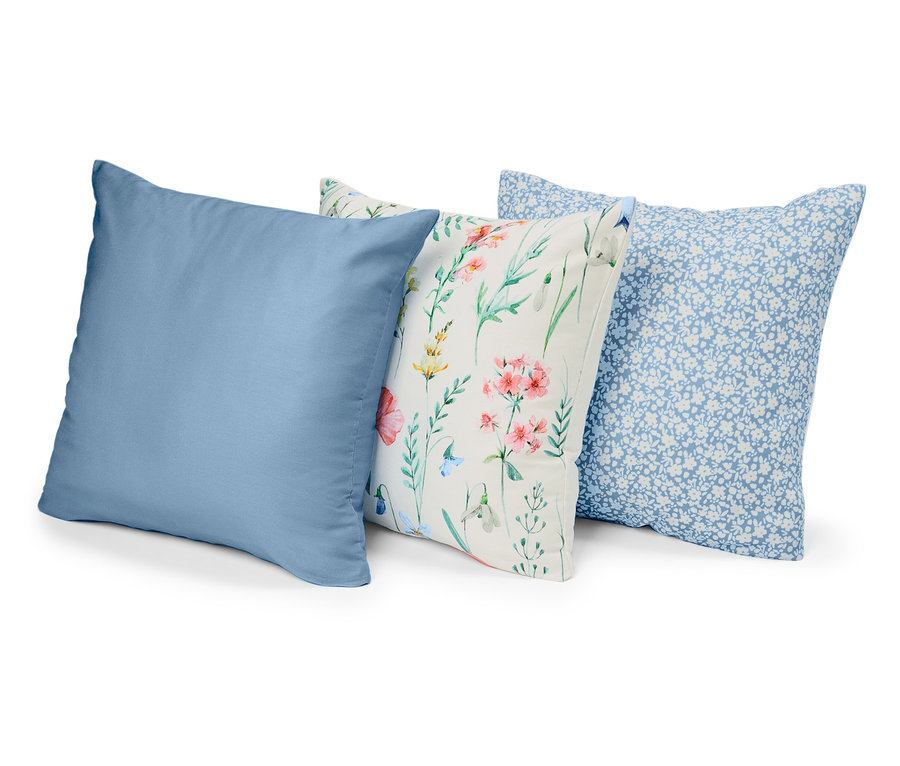 Trois coussins sont placés côte à côte : un bleu uni, un à motifs floraux et un à petites fleurs bleues sur fond bleu.