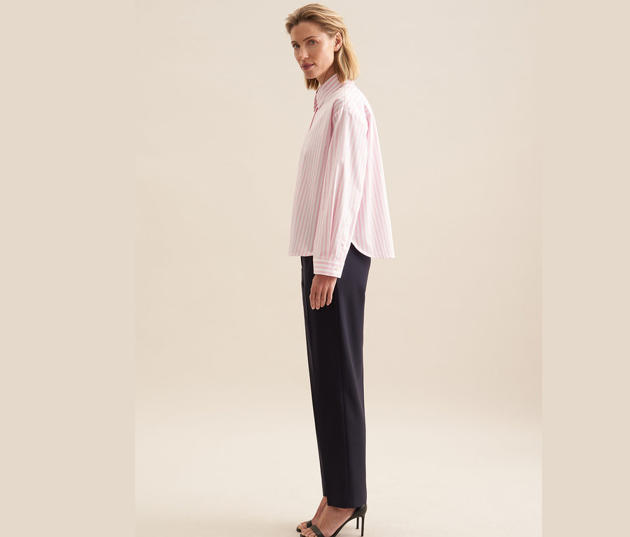 Femme posant en chemisier oversize rose Seidensticker et pantalon bleu marine.