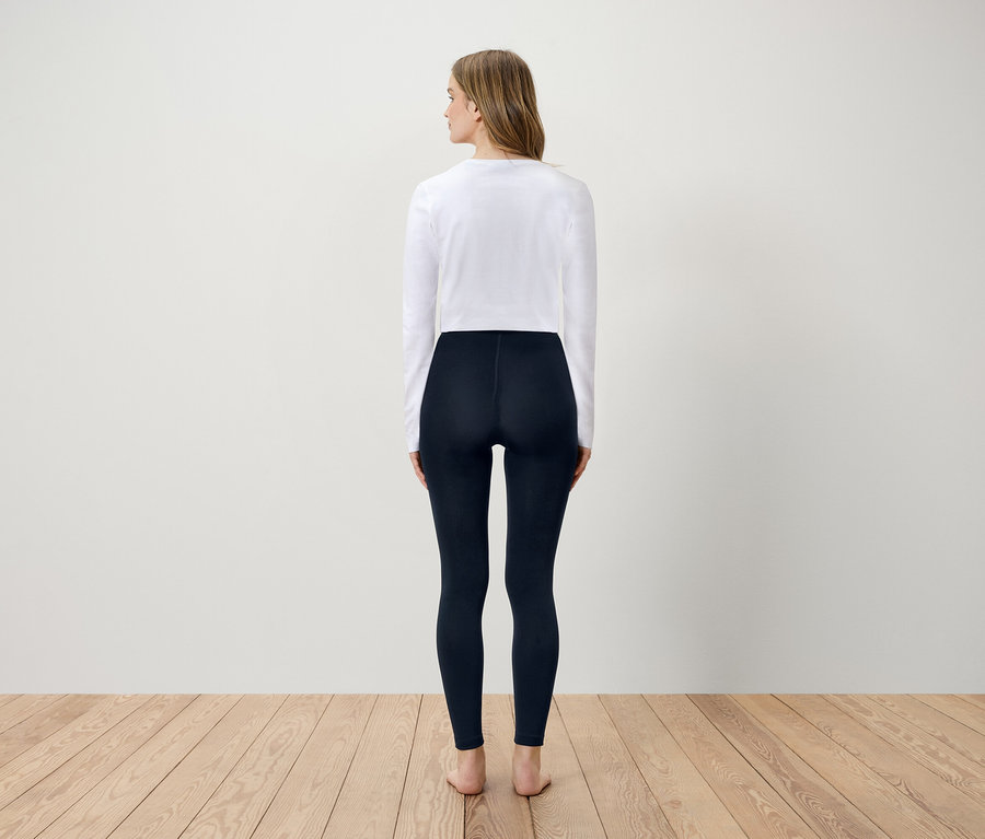 Une femme, vue de dos, porte un t-shirt blanc à manches longues et un legging bleu marine.
