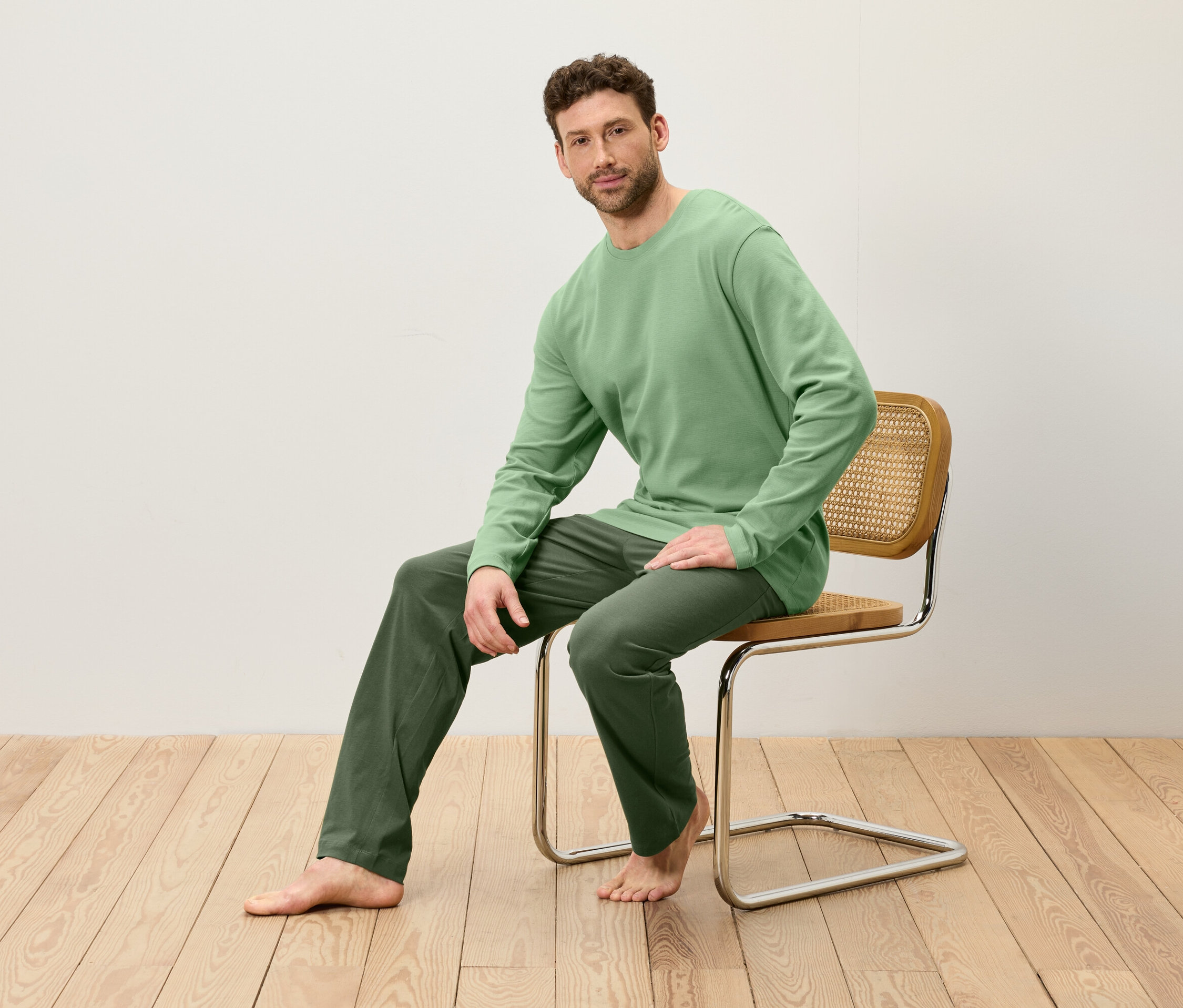 Un homme est assis sur une chaise. Il porte un t-shirt vert à manches longues et un pantalon vert.
