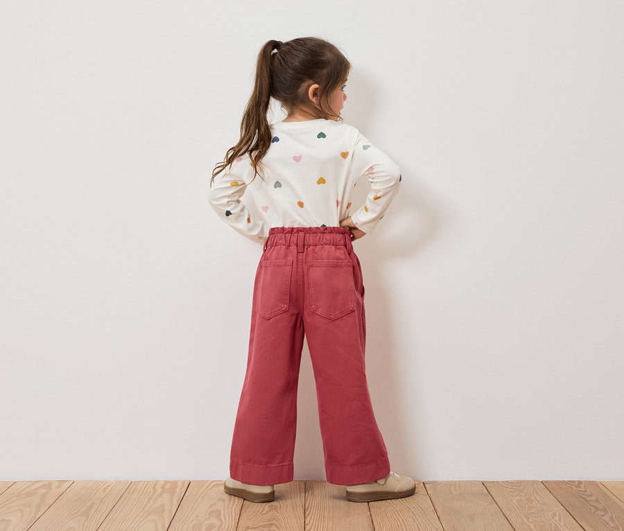 Une fillette portant un t-shirt à motifs de cœurs et un pantalon rouge se tient dos à la caméra.