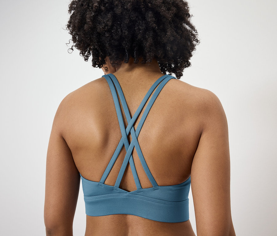 Vue arrière d'une femme aux cheveux bouclés foncés portant un soutien-gorge de sport bleu avec des bretelles croisées.