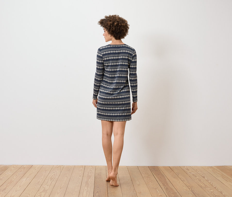 Une femme aux cheveux bouclés se tient dos à l'appareil photo et porte une robe à manches longues à motifs bleus et blancs.