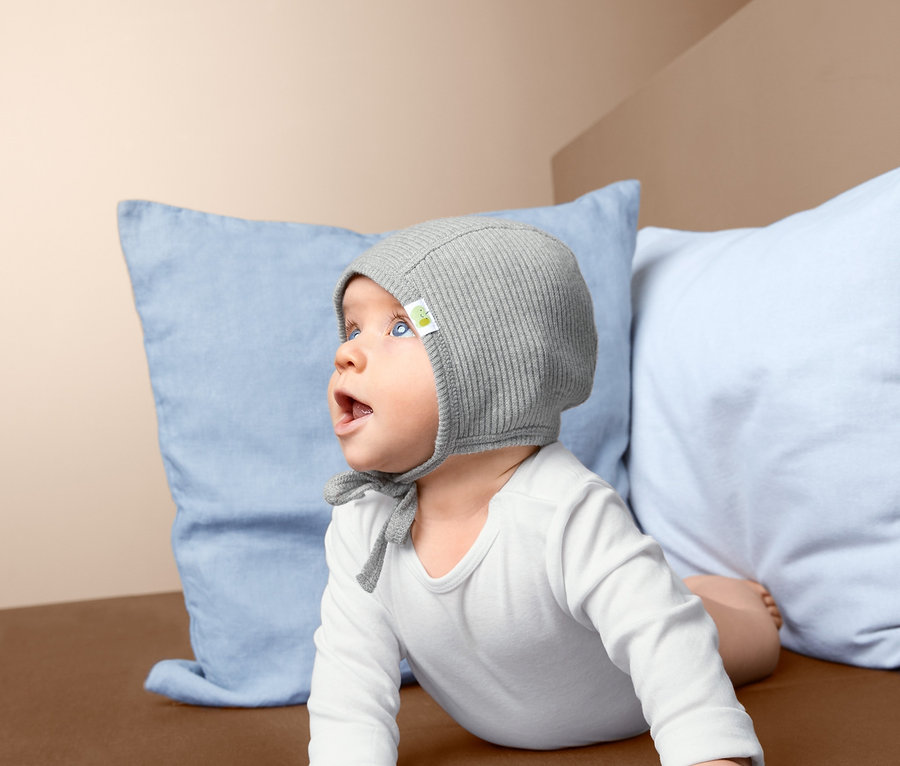 Bébé allongé sur le ventre sur une couverture marron, portant un bonnet.