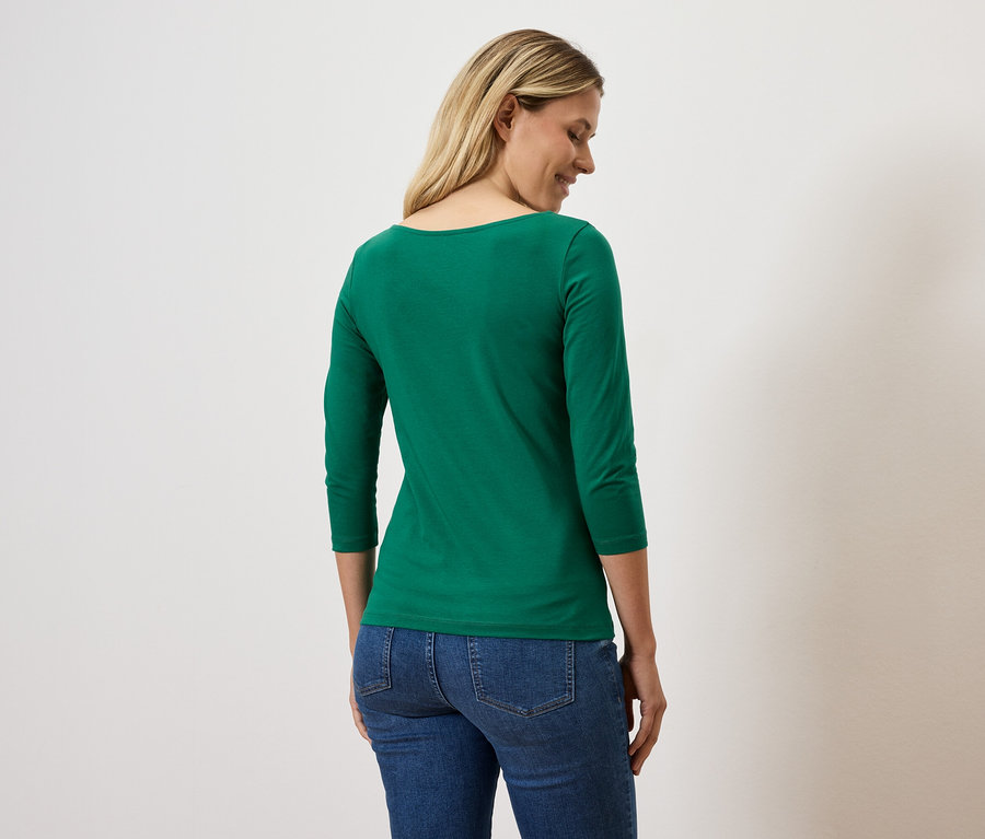 Une femme regarde sur le côté et porte un t-shirt vert à manches trois-quarts et un jean.